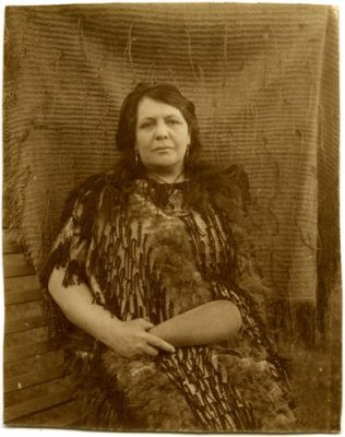 A black and white photo of Makareti as an older woman seated in front of a kaitaka garment.