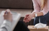 Close-up of woman's hands during counseling meeting with a professional therapist. Box of tissues and a hand of counselor blurred in the front.
